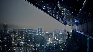 Silhouette of a person sitting on a high-rise balcony overlooking a sprawling city skyline at night with glowing windows HD wallpaper