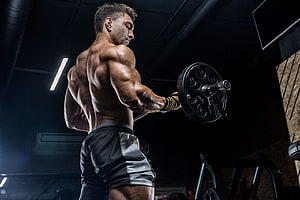Muscular Athlete Performing Barbell Curl in Dark Gym Setting HD wallpaper