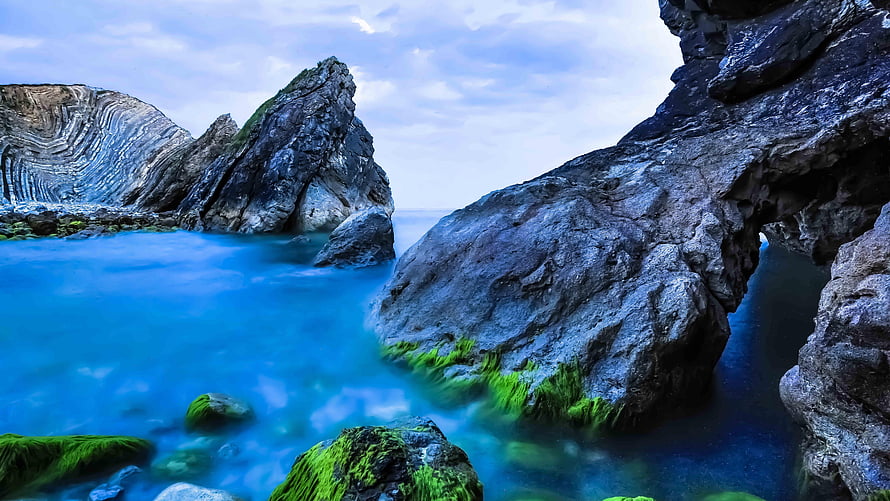 Serene Coastal Landscape With Mossy Rocks And Smooth Blue Ocean Water HD wallpaper