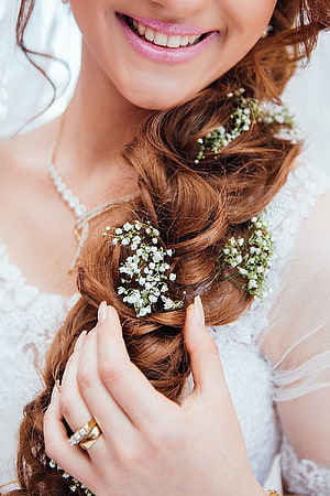 Bride with aubrieta flowers woven into a loose side braid, wearing a lace wedding dress and gold ring HD phone wallpaper