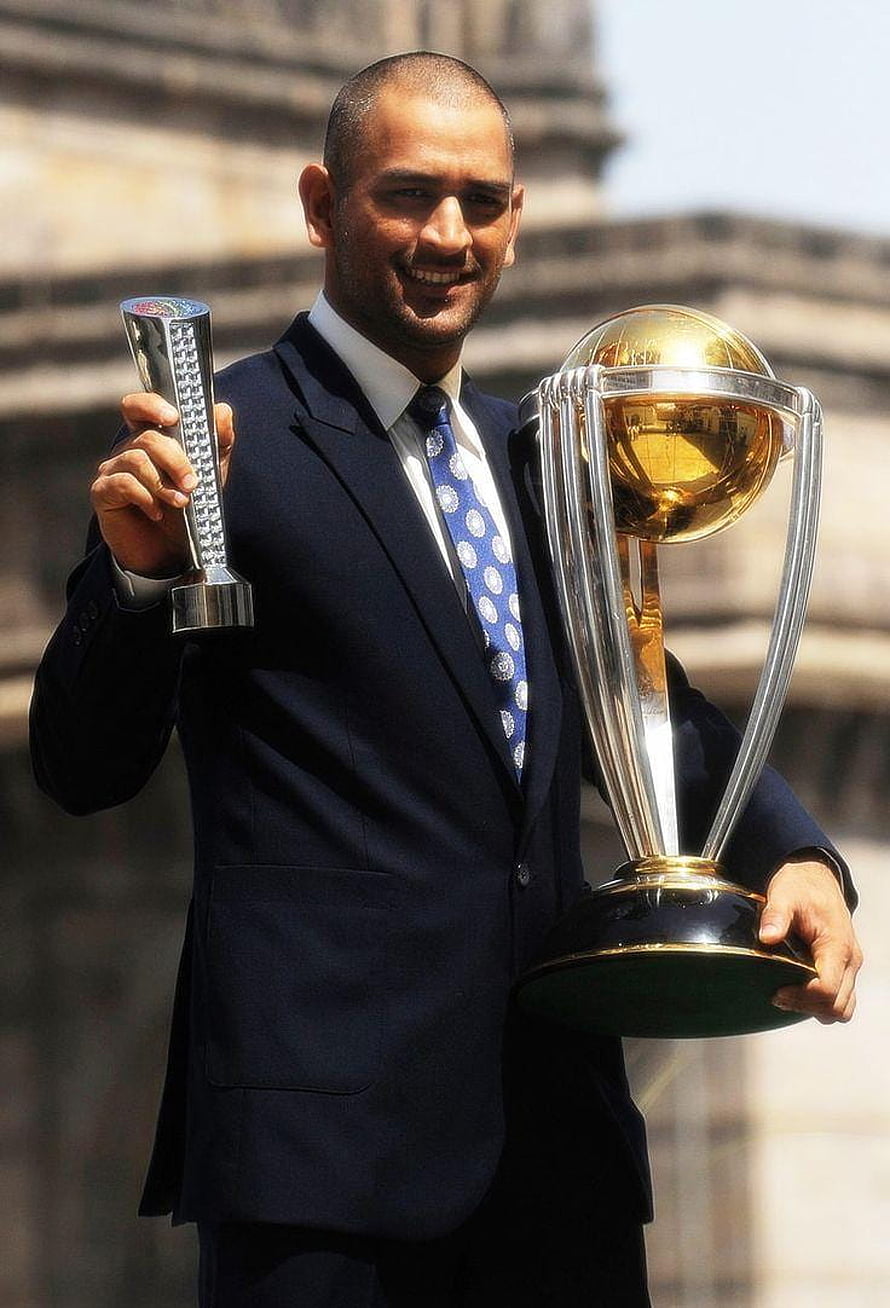 MS Dhoni holding the ICC Cricket World Cup trophy and Player of the Series award in a suit HD phone wallpaper