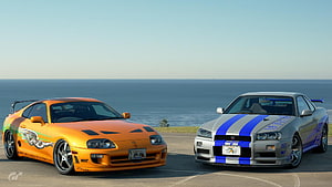 Nissan Skyline GT-R R34 and Toyota Supra RZ parked on a coastal road with ocean view HD wallpaper