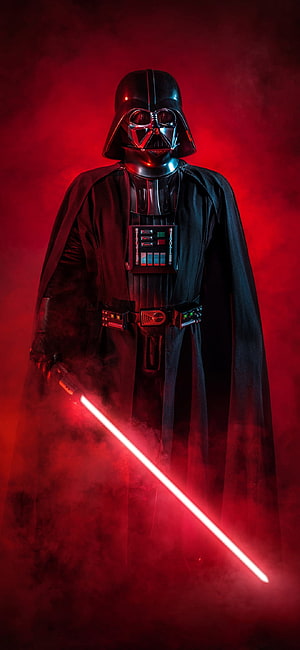 Darth Vader standing with red lightsaber in dark smoky atmosphere HD phone wallpaper