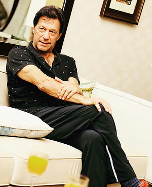 Imran Khan seated on a white sofa in a black patterned shirt and dark trousers HD phone wallpaper