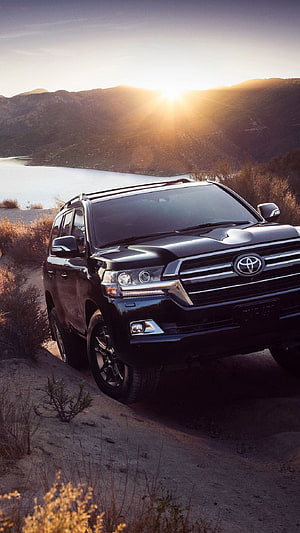 Black Toyota Land Cruiser parked on a dirt trail at sunset with a lake and mountains in the background HD phone wallpaper