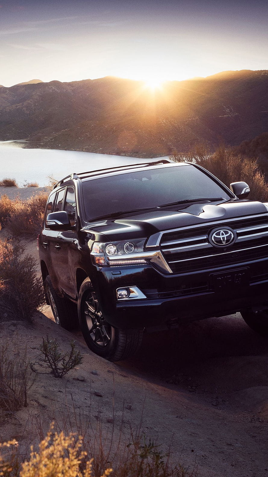 Black Toyota Land Cruiser parked on a dirt trail at sunset with a lake and mountains in the background HD phone wallpaper