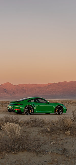 Green Porsche 911 Turbo S parked in a desert landscape at sunset with distant mountains HD phone wallpaper