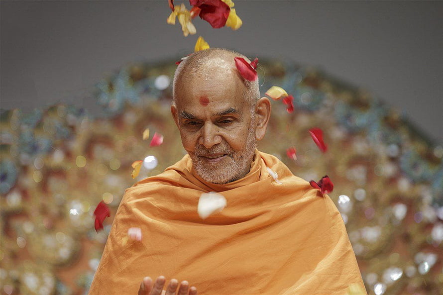 Spiritual leader in saffron robes receiving flower petals shower during religious ceremony HD wallpaper