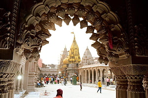Ornate stone archway framing the golden spire of a Hindu temple courtyard with visitors HD wallpaper