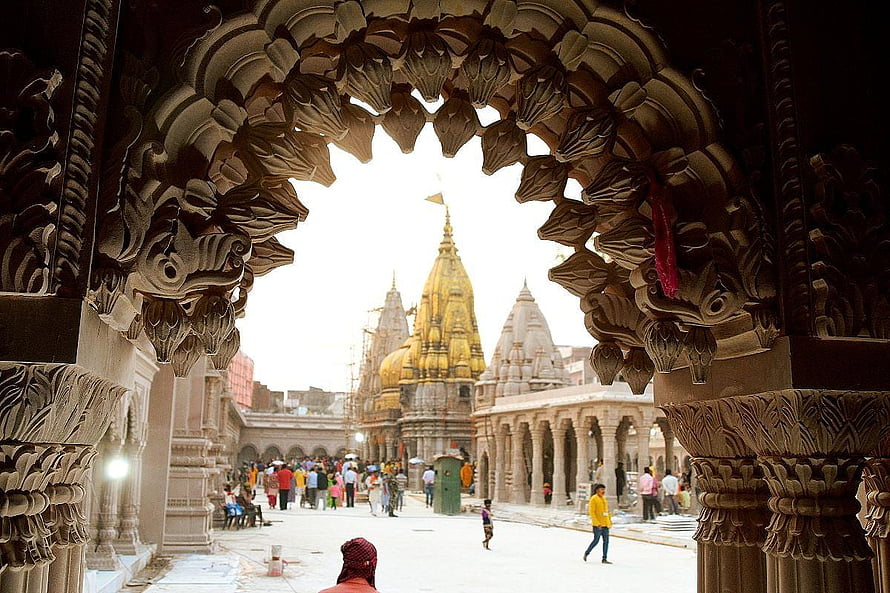 Ornate stone archway framing the golden spire of a Hindu temple courtyard with visitors HD wallpaper